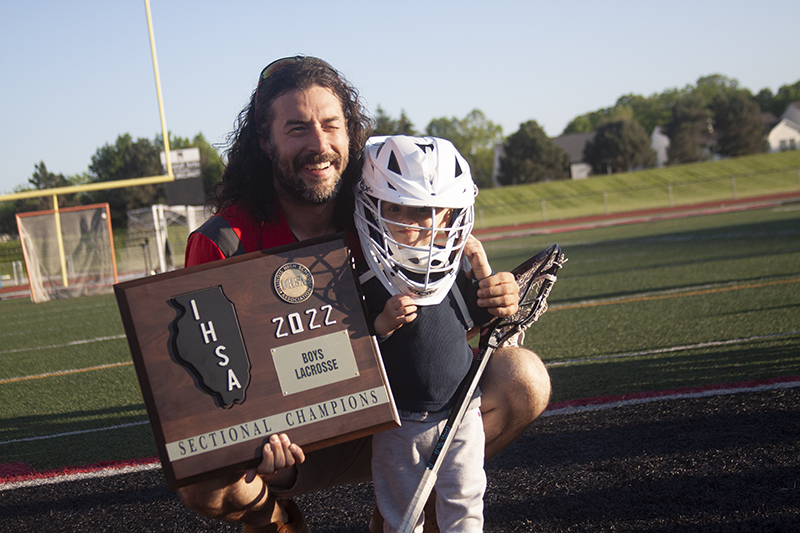 Huntley boys lacrosse head coach Dominic Saccomanno, left, and his son, Conner, show off the team's Huntley Sectional trophy earned after a 10-9 overtime Red Raiders win over Hampshire.