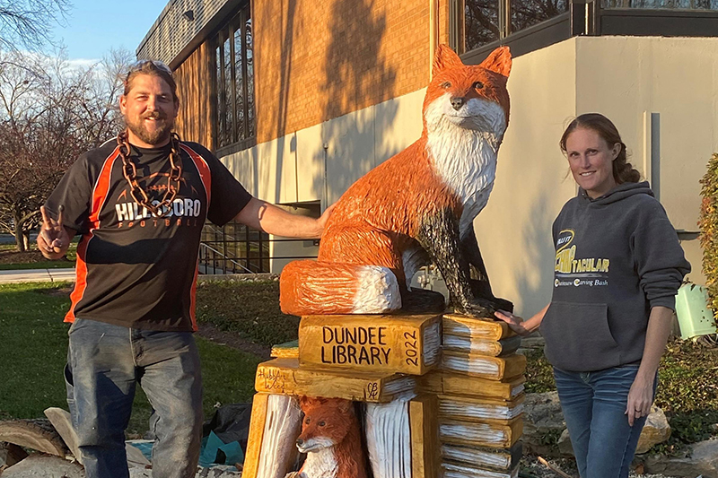 Husband and wife duo Chris (Left) and Brianne Hubbart stand beside the fox with books wood sculpture they created for the Dundee Library.