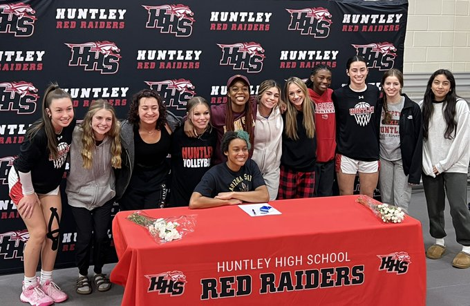 Huntley girls track-and-field team members gather to look on as senior Alexanderia Johnson signs her national letter of intent to compete for Arizona State University.