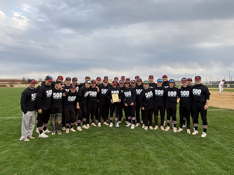 Huntley High School baseball team members gather around head coach Andy Jakubowski (holding plaque) after he won his 500th career victory April 24. The Red Raiders downed Jacobs 12-2.