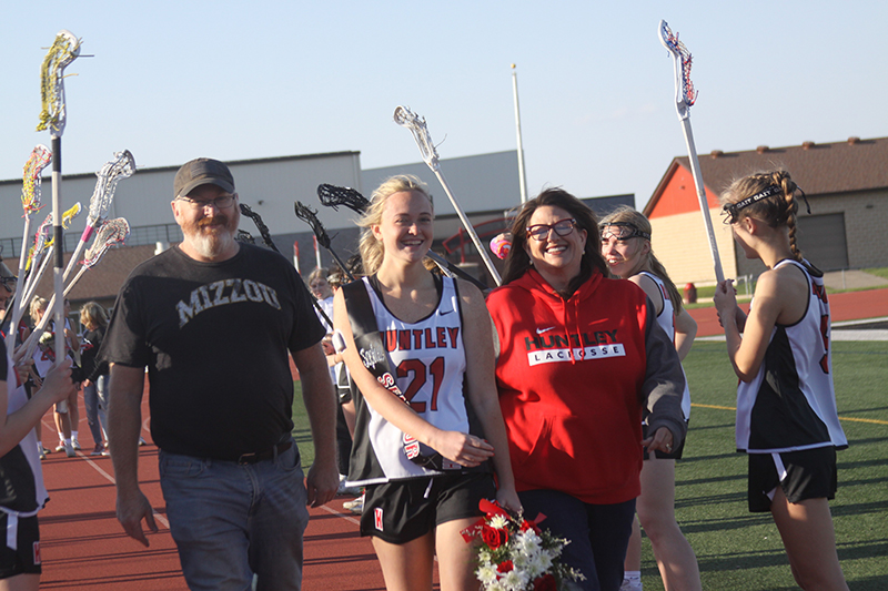 Huntley senior Sophia Zion and parents Mark and Stacy walk through a salute on Red Raiders' girls lacrosse on senior night.