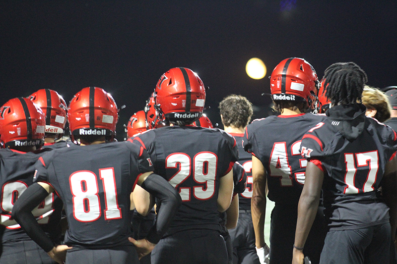 Huntley football players look on from the sideline, in the Pairie Ridge game, as a late-summer moon hovers above Red Raider Stadium.